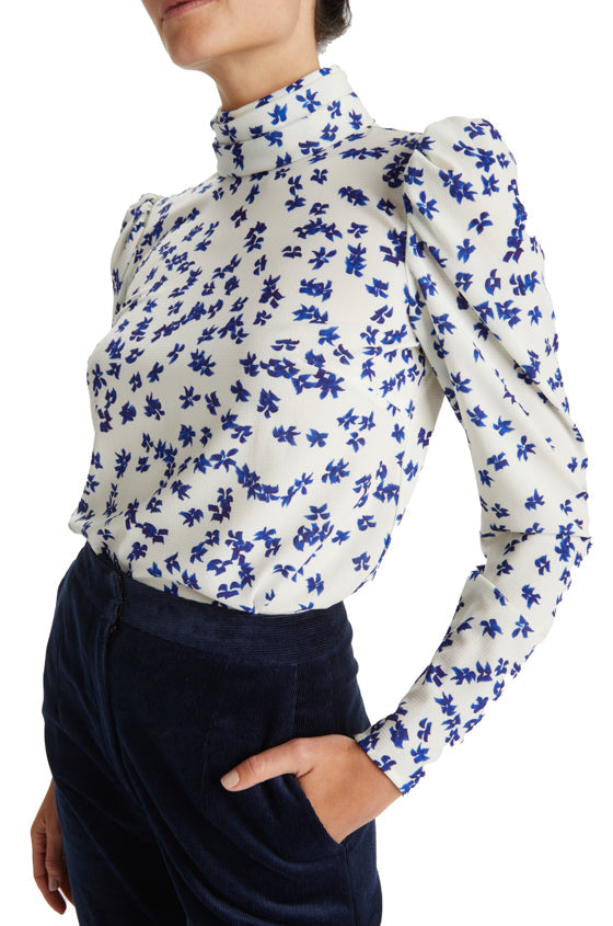 Woman in silk white and blue floral crepe blouse with high neck and long sleeves.